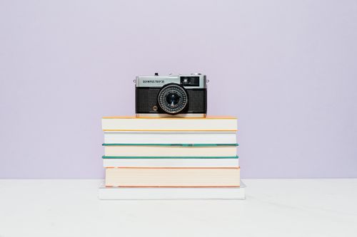 Free A classic Olympus Trip 35 camera sits atop a stack of books against a pastel background. Stock Photo