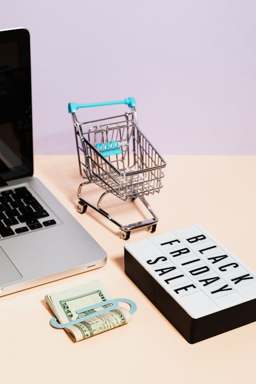 A Black Friday Sale Signage Beside a Miniature Shopping Cart and Clipped Money