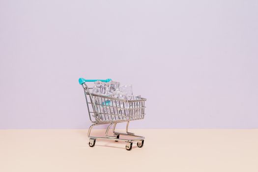 A small shopping cart filled with ice cubes against a pastel backdrop, perfect for retail or concept themes.