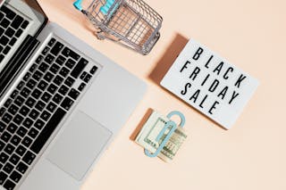 Free Top View of Silver Macbook Beside a Shopping Cart and Black Friday Sale Signage Stock Photo
