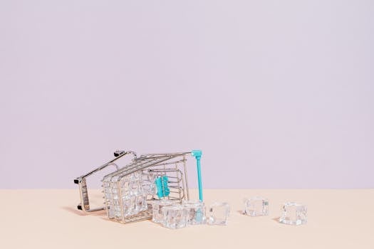 Tipped shopping cart with ice cubes on pastel background, offering creative copy space.