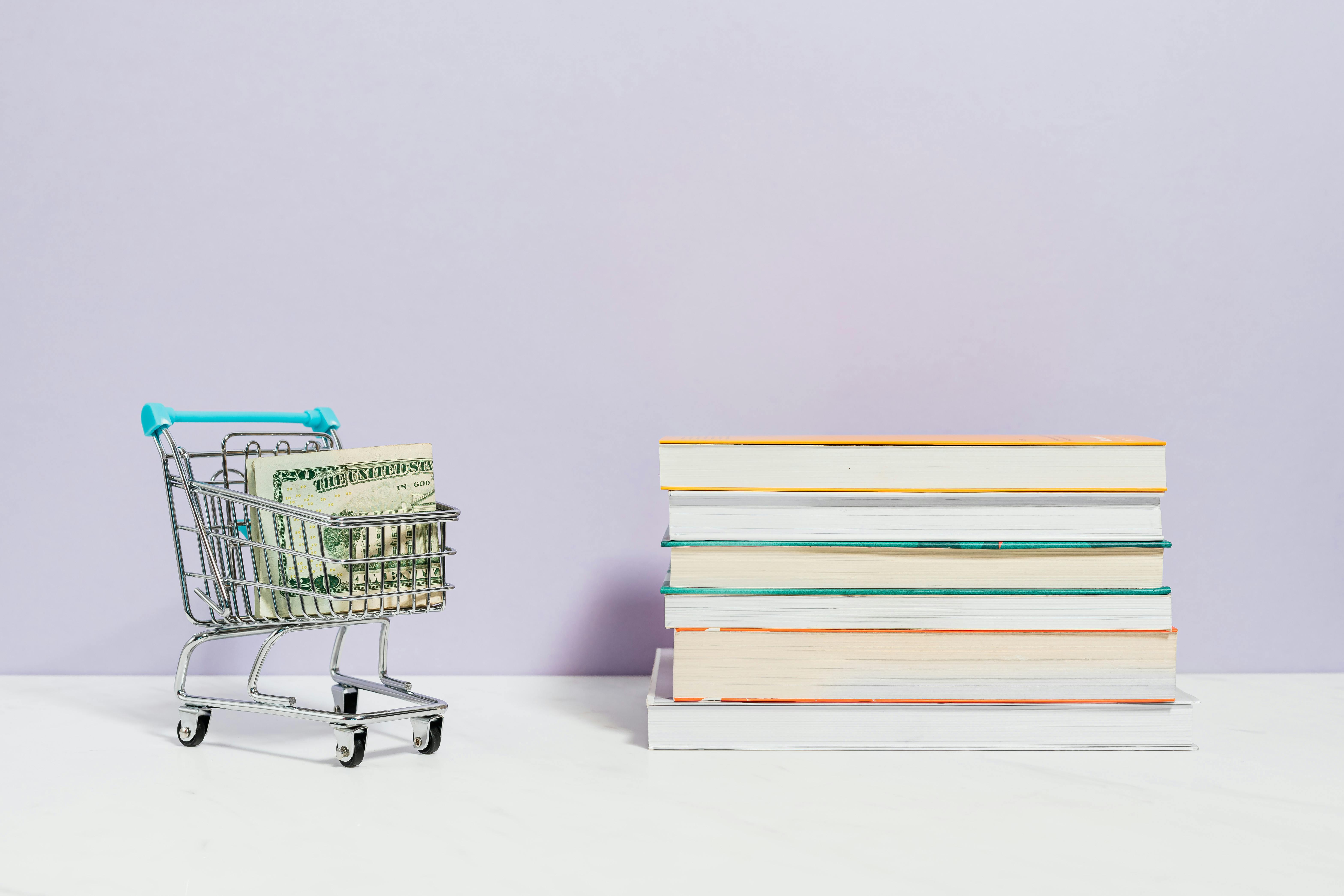 stack of books beside a shopping cart with cash money
