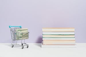 Stack of Books Beside A Shopping Cart With Cash Money