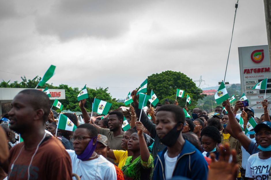 Un grupo de personas protestando en las calles, agitando banderas nigerianas bajo un cielo nublado.