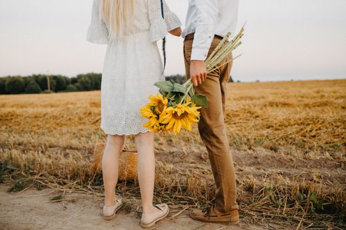 Free A couple holding sunflowers stands in a golden field. Perfect for depicting love and nature. Stock Photo