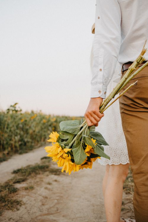 Free A couple walks on a path holding a sunflower bouquet, symbolizing love and nature. Stock Photo