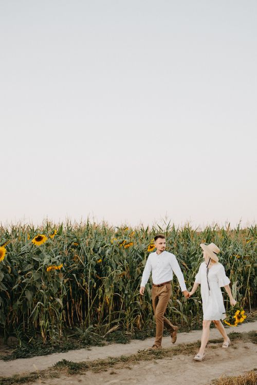 Free A couple walking hand in hand through a sunflower field on a sunny day. Stock Photo