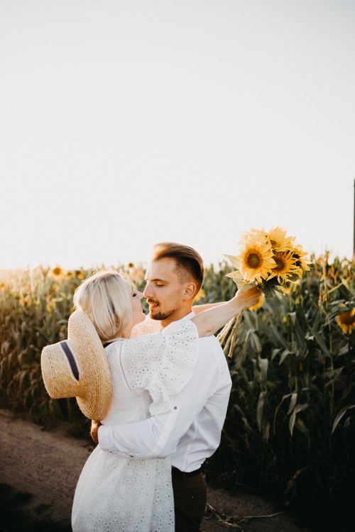 Free A couple sharing a romantic moment while embracing in a sunflower field during sunset. Stock Photo