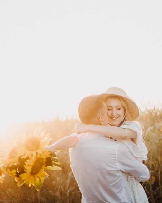 A couple embraces lovingly in a sunflower field during sunset, creating a warm and affectionate moment.