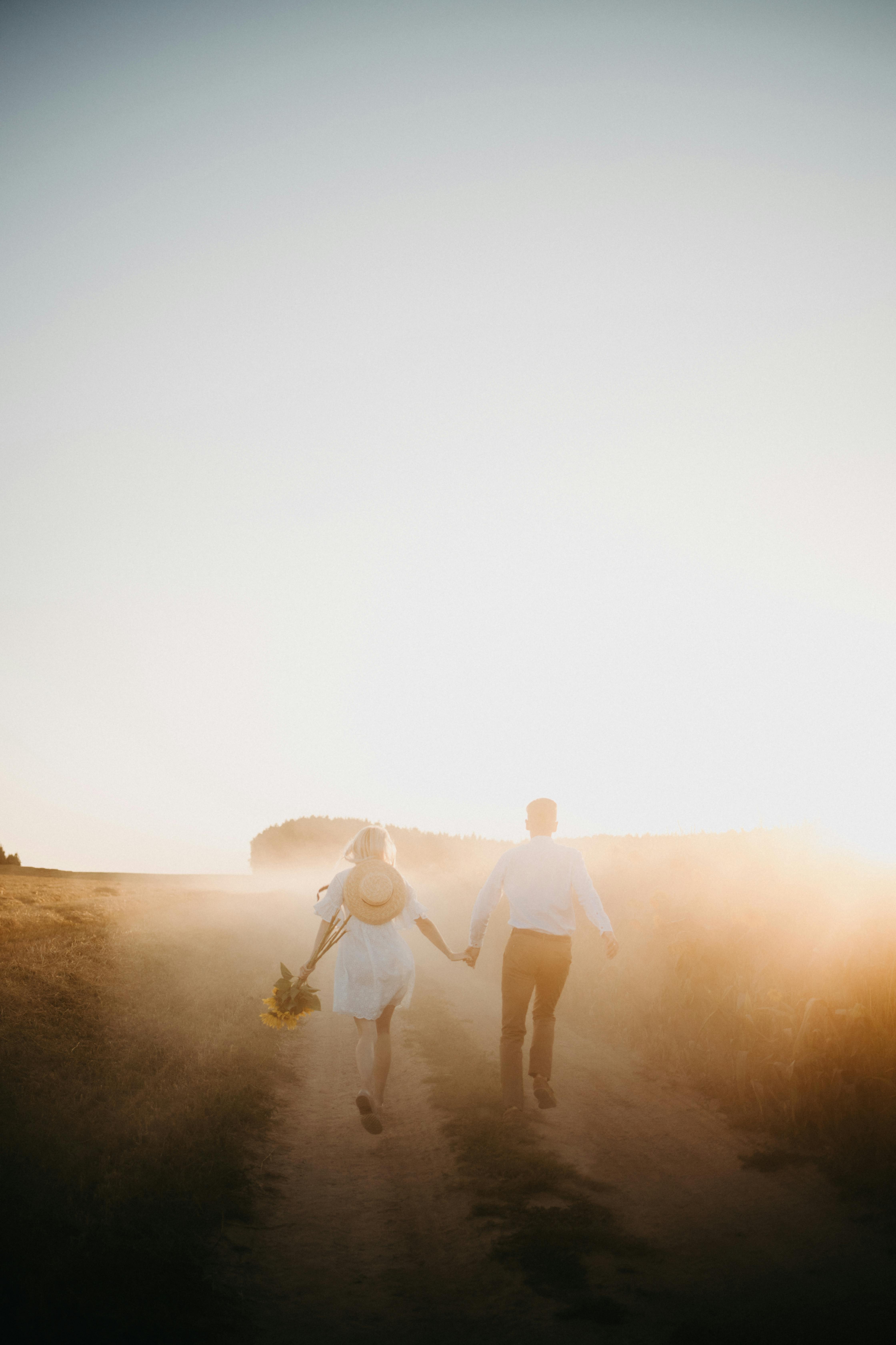 man and woman walking on sand during sunset