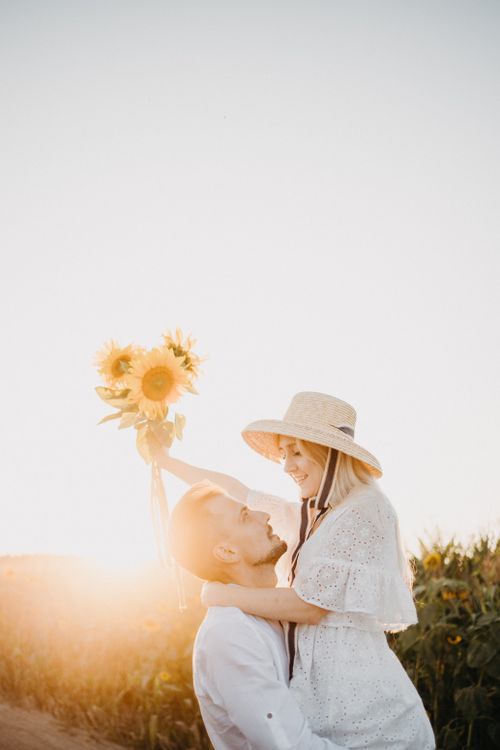 Free Couple enjoying a romantic moment with sunflowers at sunset in a field. Stock Photo