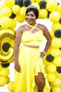 Cheerful African American female in festive outfit with tiara on head looking at camera near bright balloons