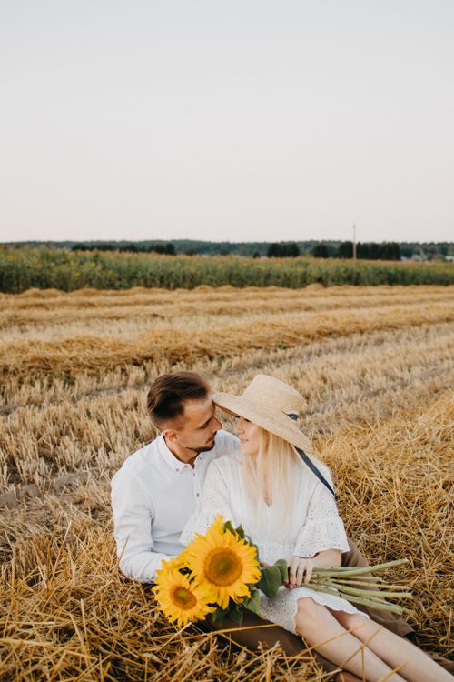 Free A couple enjoys a romantic moment in a wheat field, holding sunflowers. Stock Photo