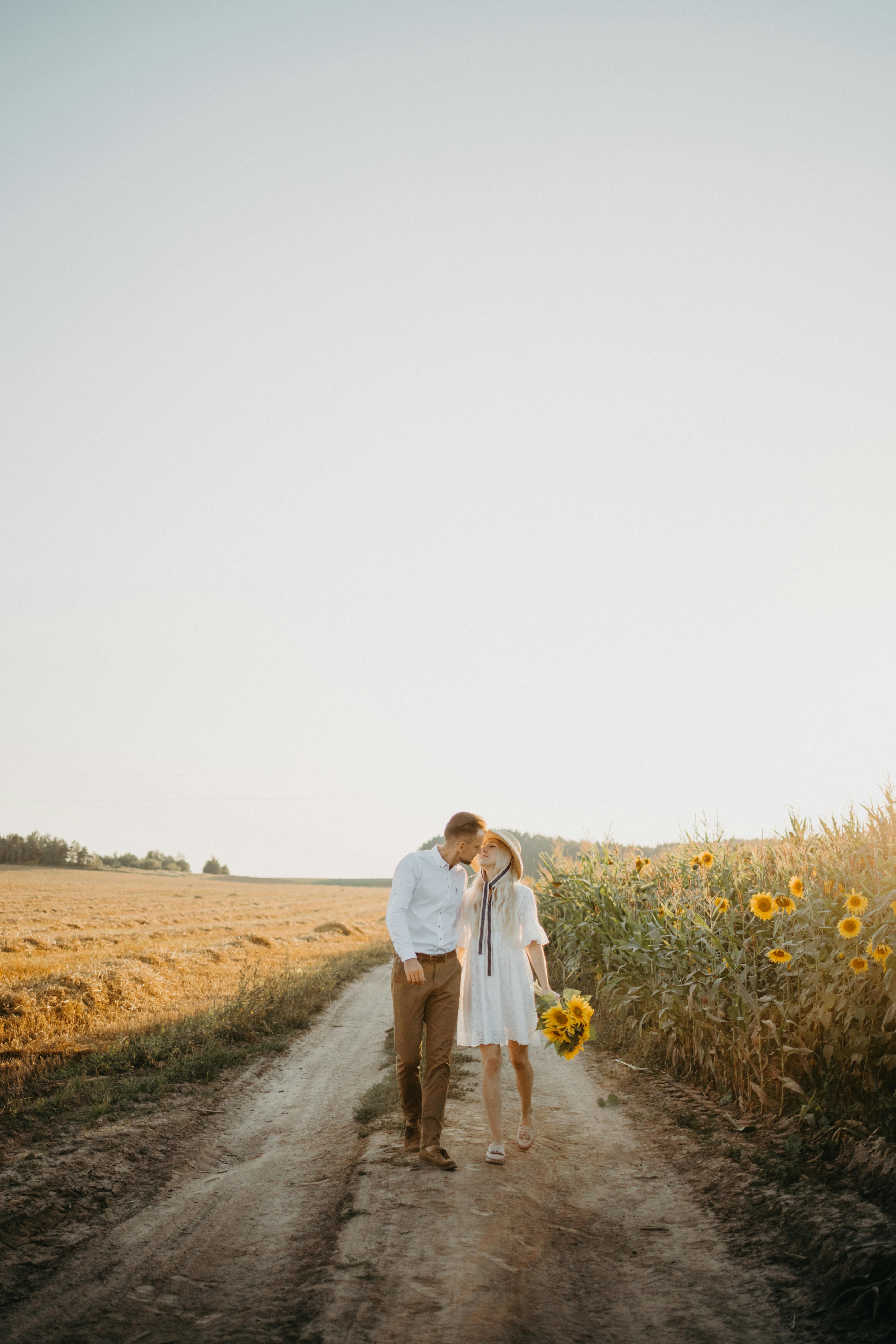 man and woman walking on dirt road between green grass field