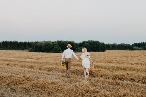 Free Couple holding hands and walking through a scenic wheat field, capturing a moment of romance and freedom. Stock Photo
