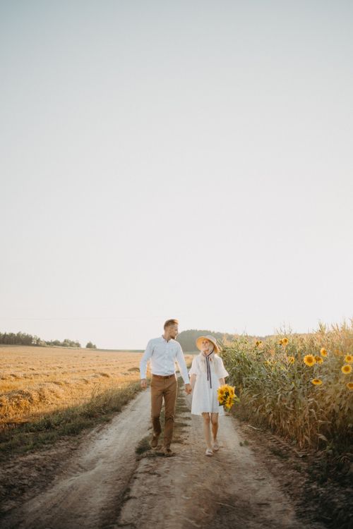 Free A couple strolls hand in hand through a sunflower field on a sunny day. Stock Photo