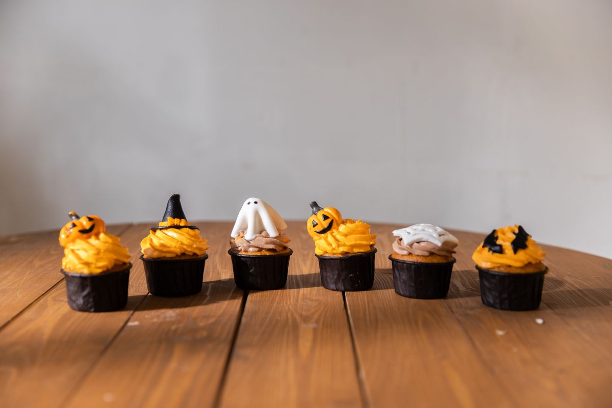 Halloween cupcakes decorated with ghosts and pumpkins on a party table.