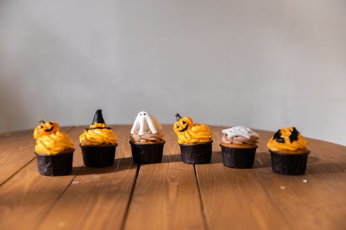 Free Halloween cupcakes decorated with ghosts and pumpkins on a wooden table, perfect for seasonal festivities. Stock Photo
