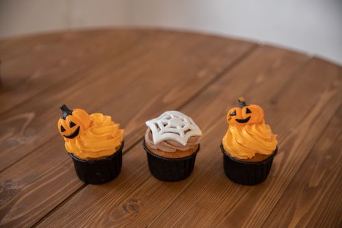 Free Three Halloween-themed cupcakes with pumpkin and spider web designs on a wooden table. Stock Photo