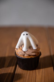 A cute Halloween cupcake topped with ghost-shaped fondant and creamy frosting, perfect for festive celebrations.