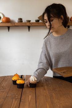 一个穿着毛衣的女人在室内用万圣节主题的纸杯蛋糕装饰木桌