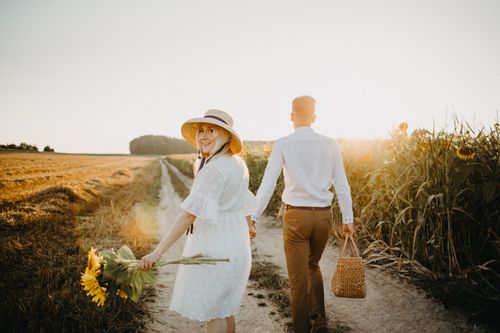 Free A couple walking hand in hand through a sunny sunflower field, capturing romance and nature. Stock Photo