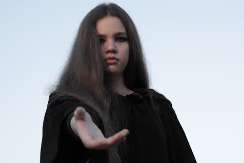 Calm wistful woman in black cloak offering hand
