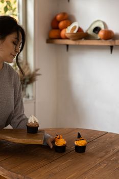A woman presents Halloween-themed cupcakes on a wooden table, adding festive charm to the room.