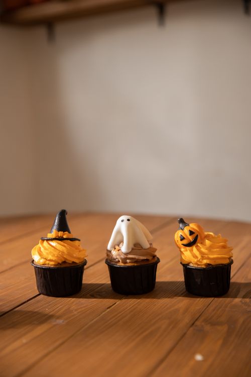 Free Three Halloween cupcakes featuring witch hat, ghost, and pumpkin designs on a wooden table. Stock Photo