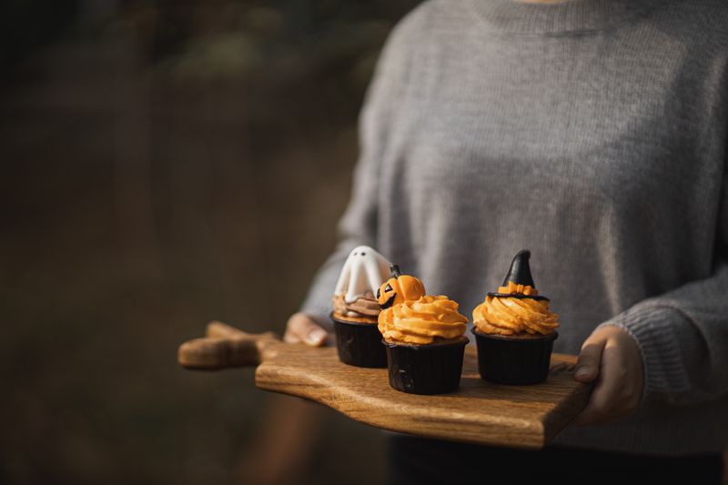Three Halloween-themed cupcakes with spooky designs on a wooden tray being held.