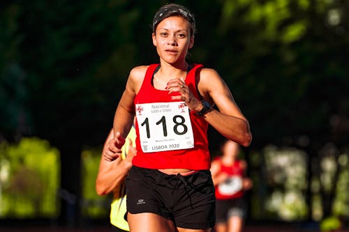 Free Determined ethnic sportswoman in active wear with numbers running during track and field competition while looking at camera Stock Photo