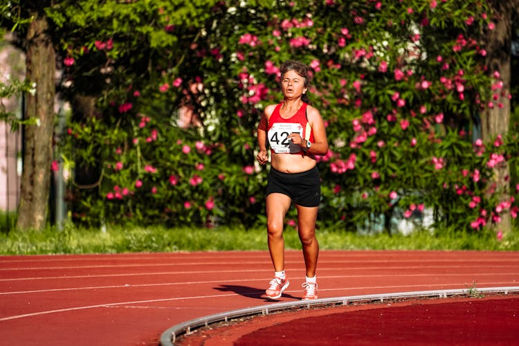 Mature Sportswoman Running On Race Track In Stadium