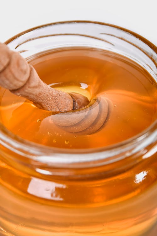 Glass Jar with Yellow Honey and Wooden Stirring Tool