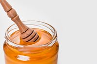 Glass jar of honey with a wooden dipper on a white background — photo by Adonyi Gábor on Pexels