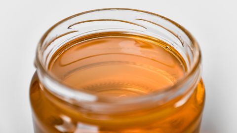 Close-up of a jar filled with golden honey, emphasizing its smooth texture and shimmering hue.