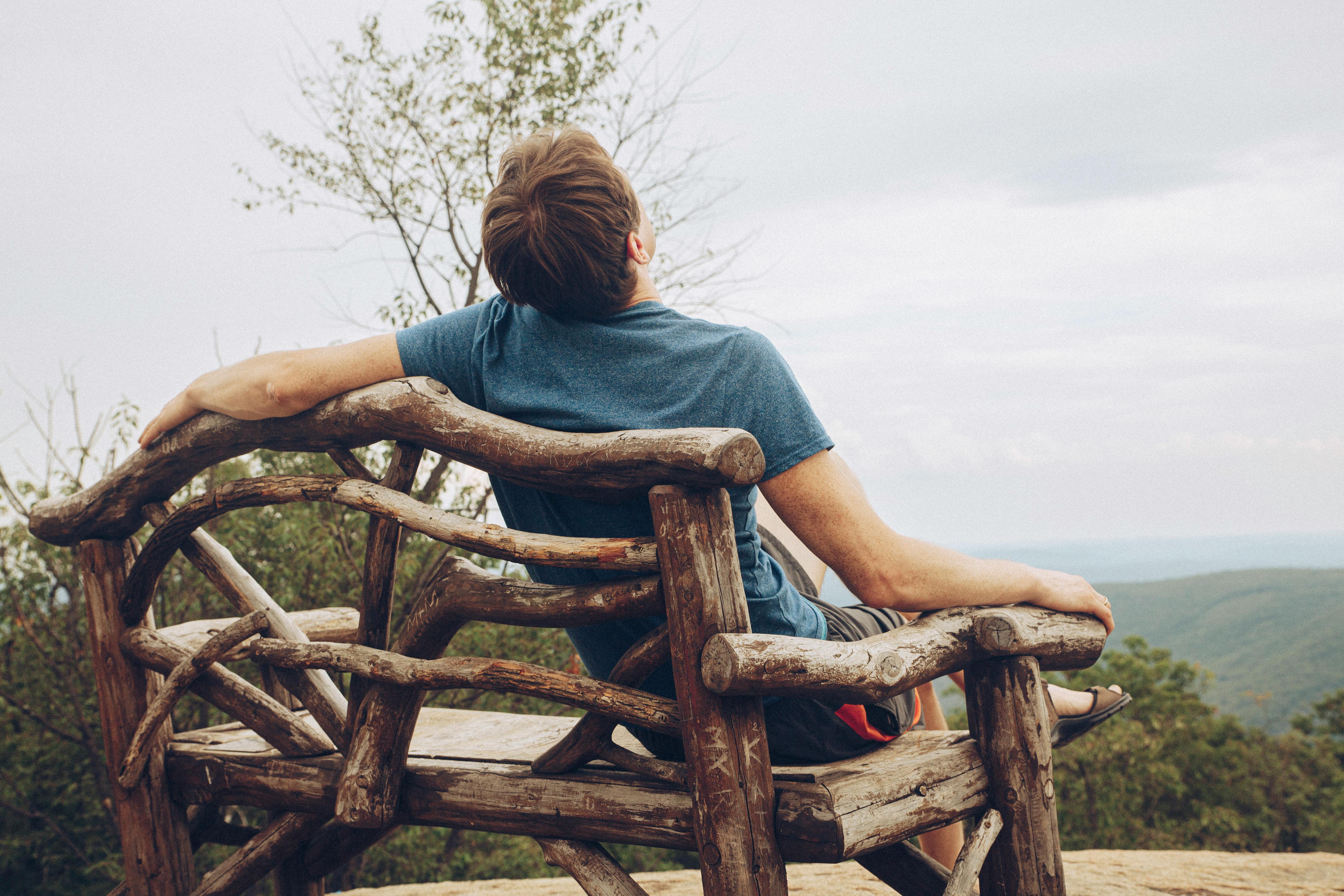 A man enjoys a tranquil moment on a wooden bench overlooking a scenic mountain landscape in New York.