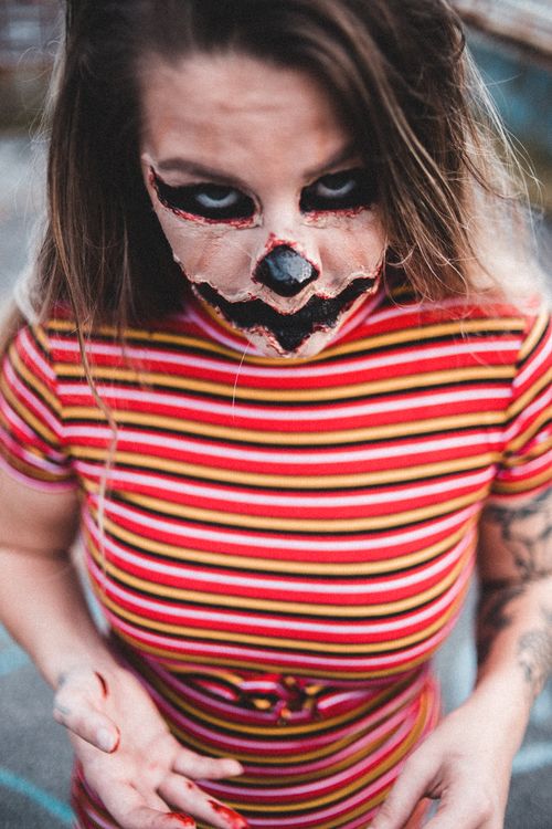 Free From above of female with scary greasepaint looking at camera while standing with blood on hand with blurred background outside Stock Photo
