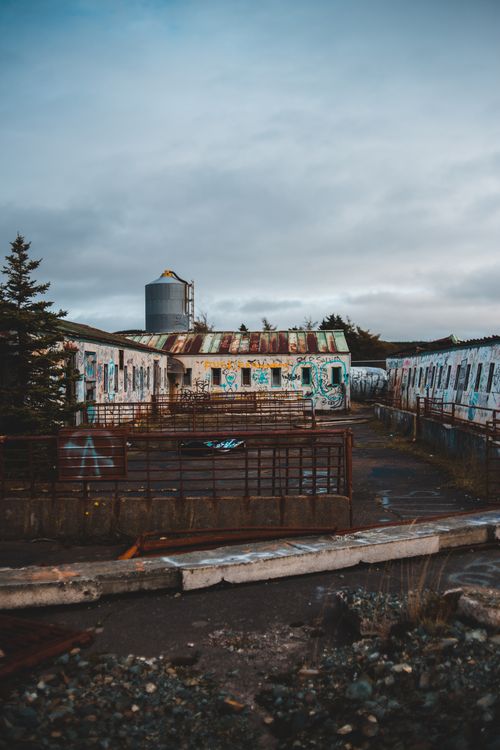 Free Abandoned shabby house with graffiti on walls located in neglected district with metal tank in distance in street against cloudy sky Stock Photo