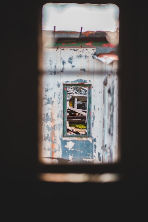 Free Weathered building facade with worn out wooden panels through window frame in daylight Stock Photo