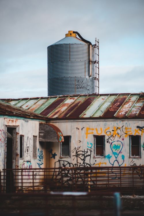 Free Exterior of metal tower and forgotten shabby building with graffiti on walls under gloomy sky Stock Photo
