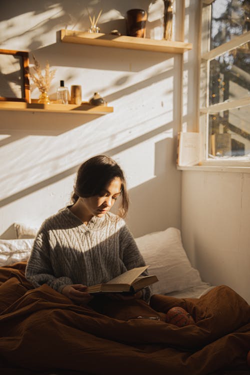 책을 읽고 그녀의 침대에 앉아 회색 긴 소매 셔츠에 여자