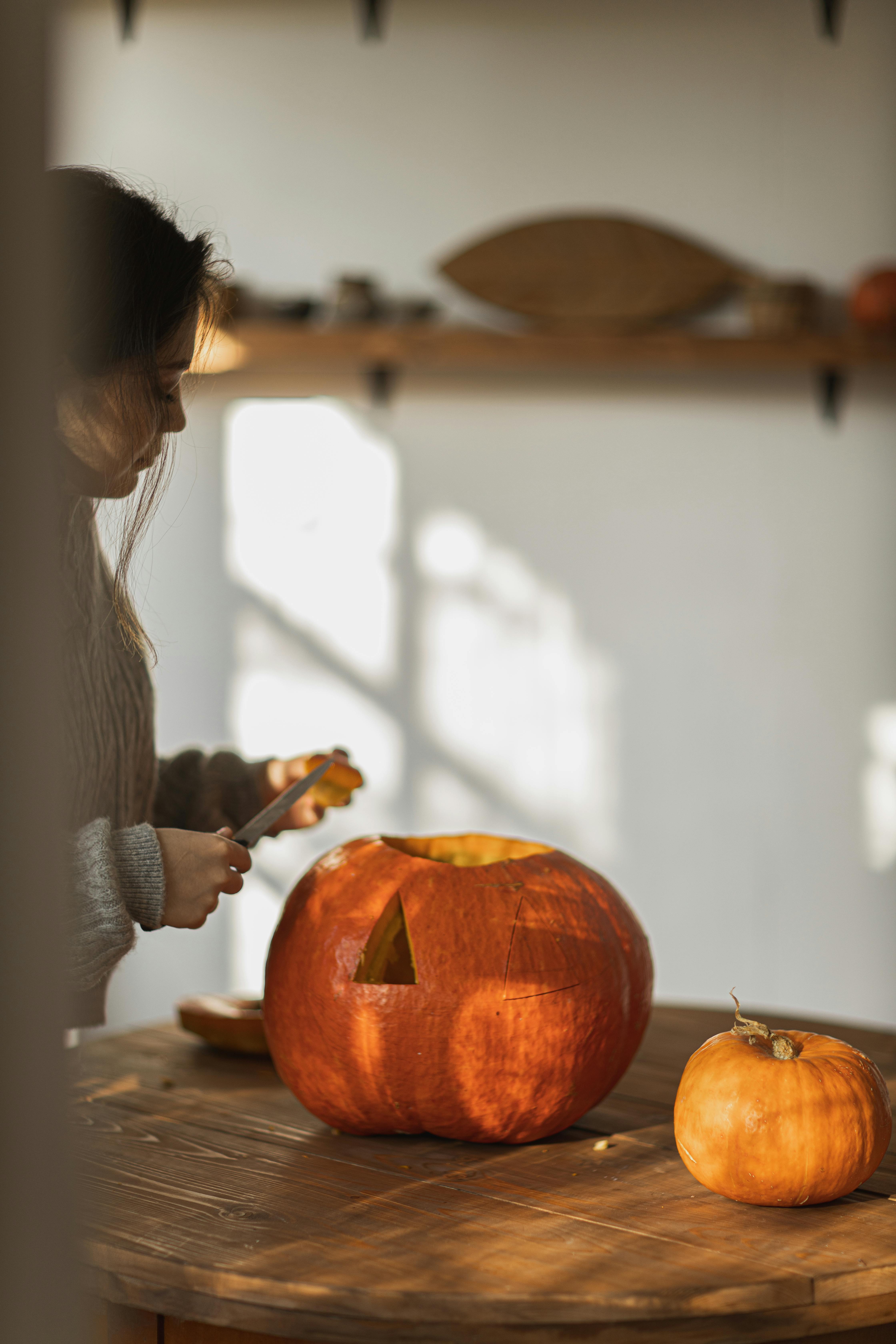 woman in gray long sleeve shirt carving a big orange pumpkin