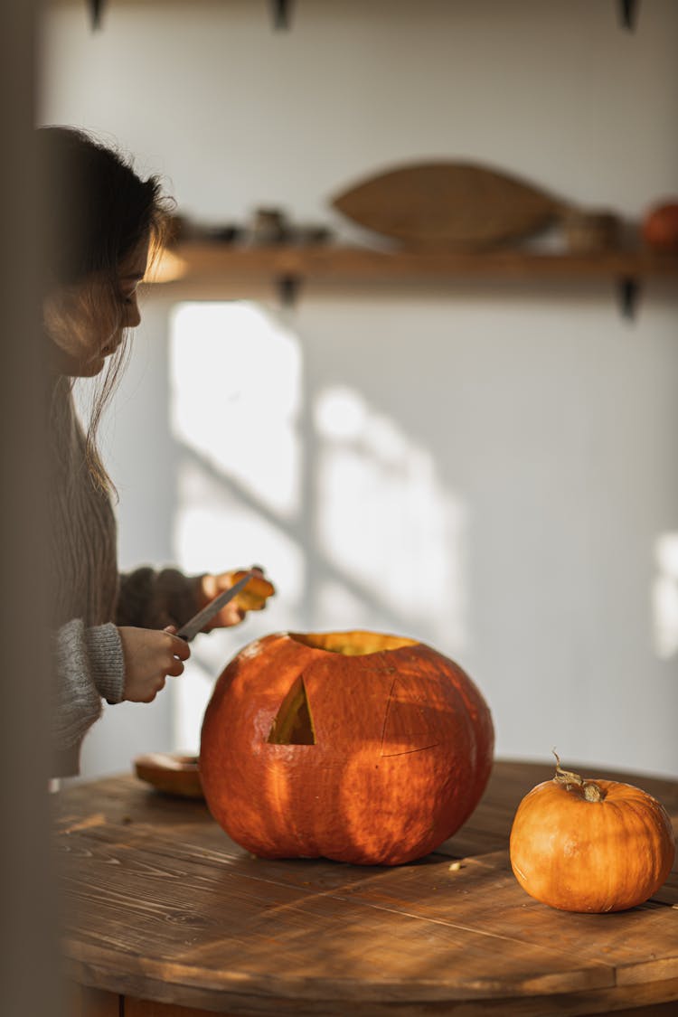 Woman In Gray Long Sleeve Shirt Carving A Big Orange Pumpkin