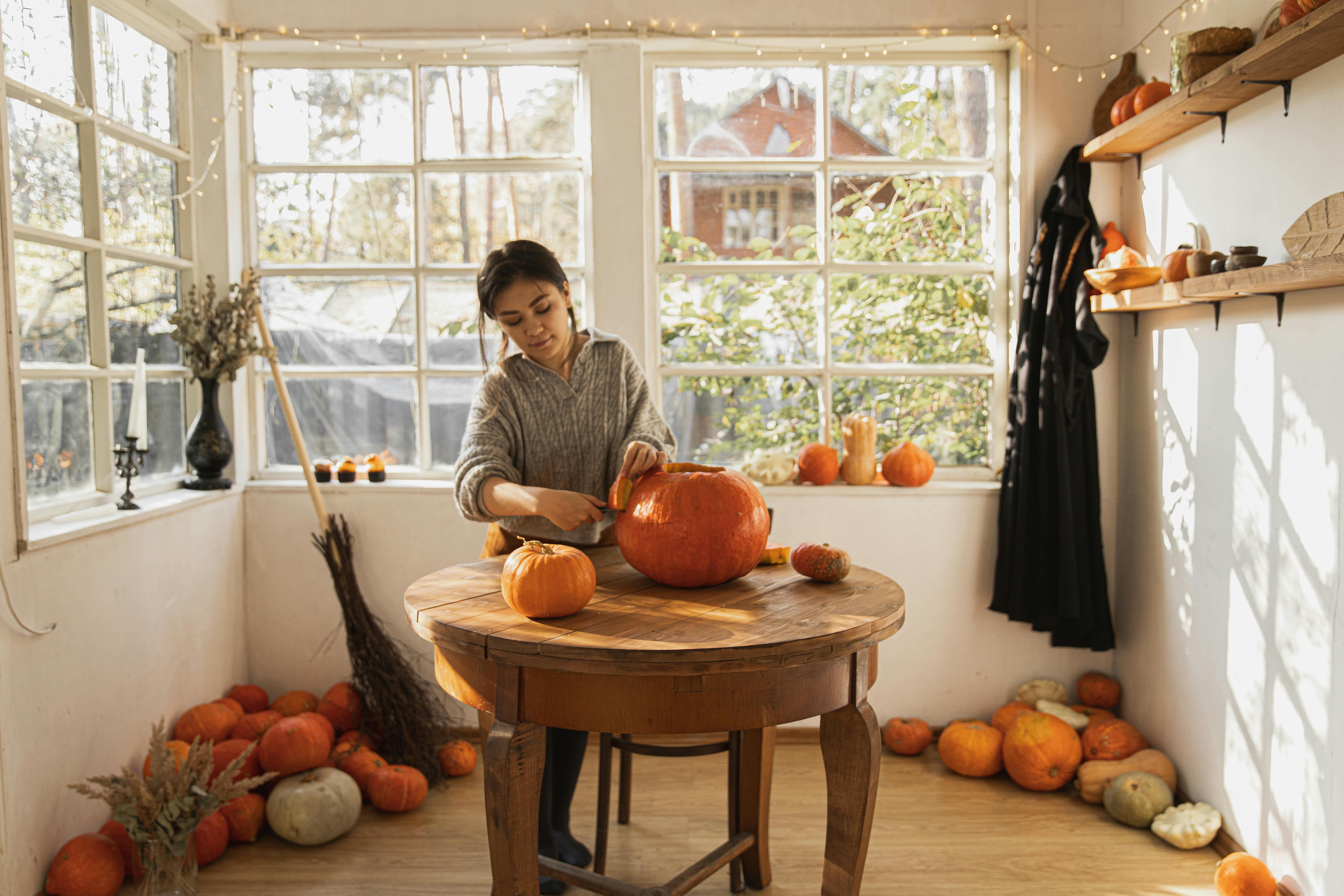 woman in gray long sleeve shirt carving a big orange pumpkin