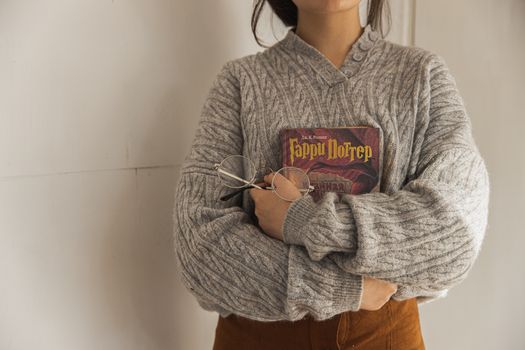 秋天，一位穿着针织衫、戴着眼镜的女人在室内拿着一本书