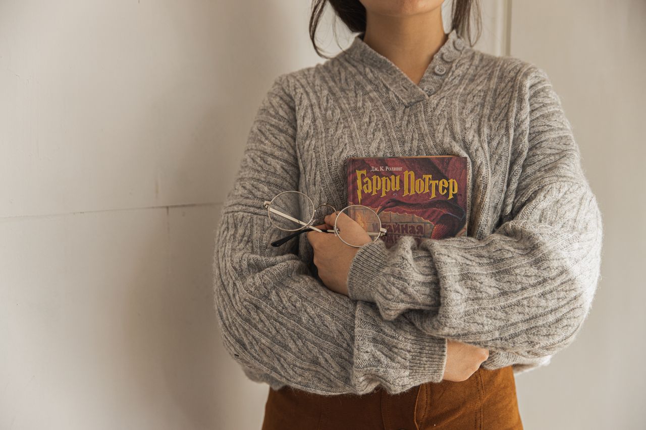 Woman in an oversized gray cable-knit sweater holding a book