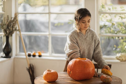 Woman in Gray Sweater Standing Near Brown Wooden Table With Pumpkin