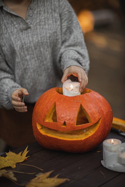 Person in Gray Long Sleeve Shirt Putting Candle in the Jack O Lantern