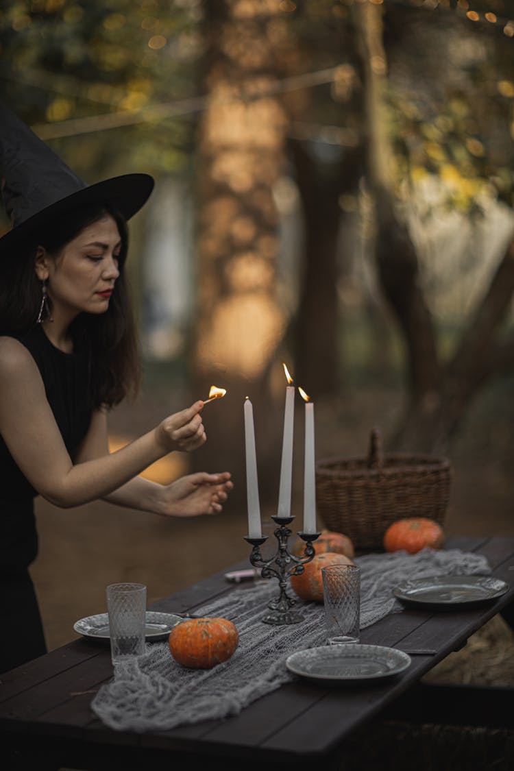 Woman In A Witch Costume Lighting Candles On The Table