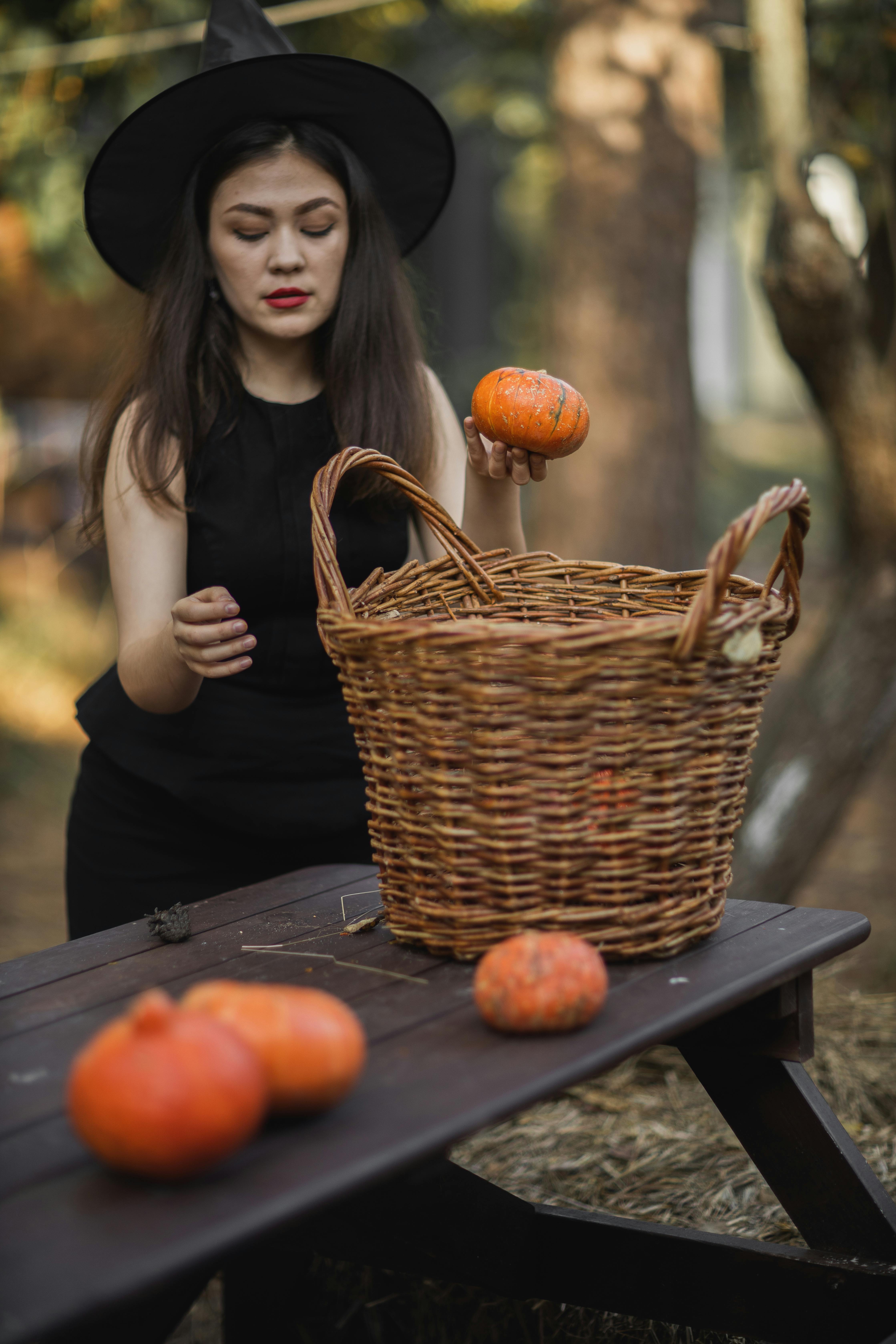 woman in black dress holding pumpkin beside brown woven basket